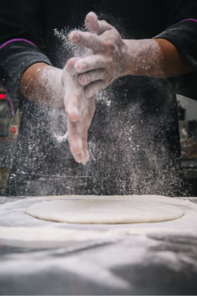Kokk slår av mel fra hendene over en pizzadeig