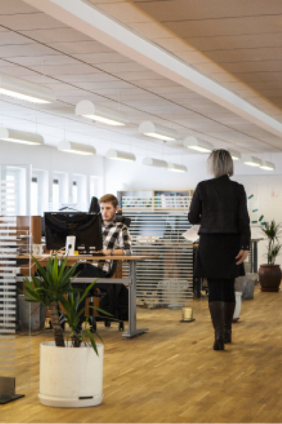 Kvinne går mot mann som sitter foran datamaskin
